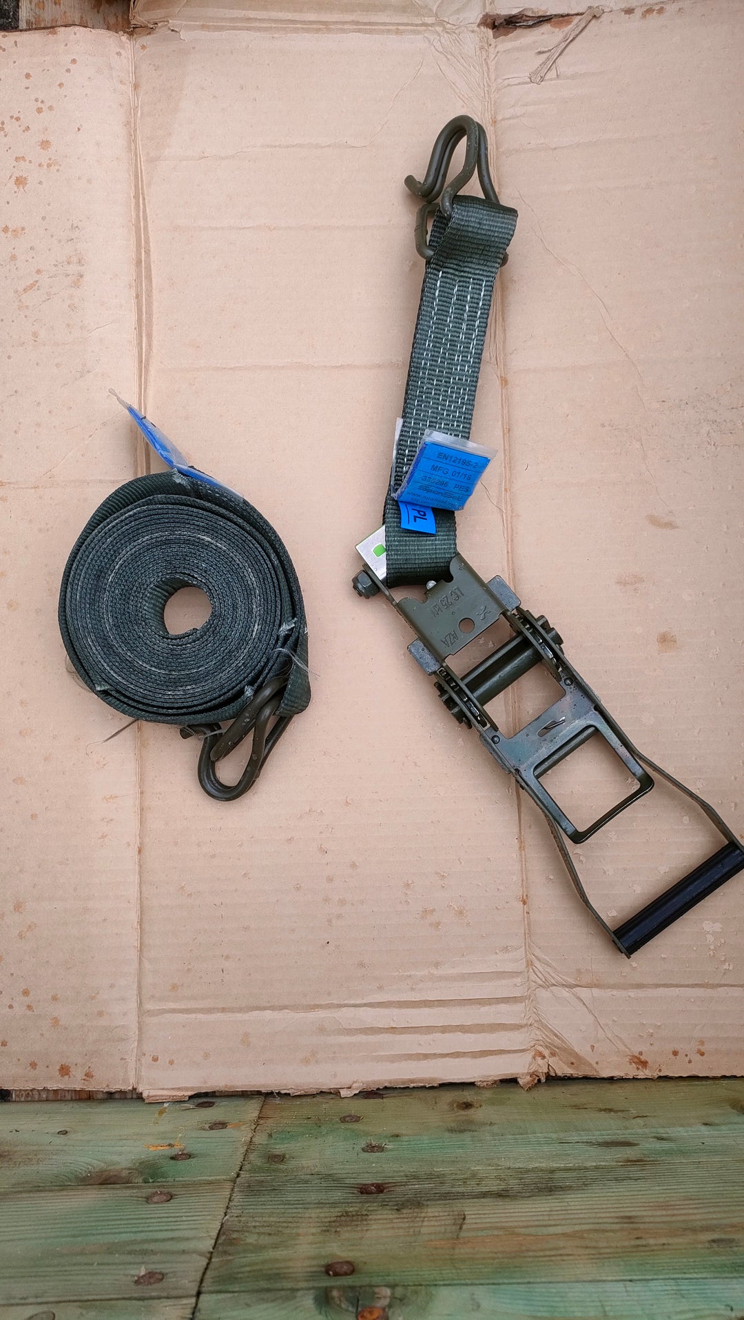 long strap coiled up into a roll and large metal ratchet attachment on cardboard background