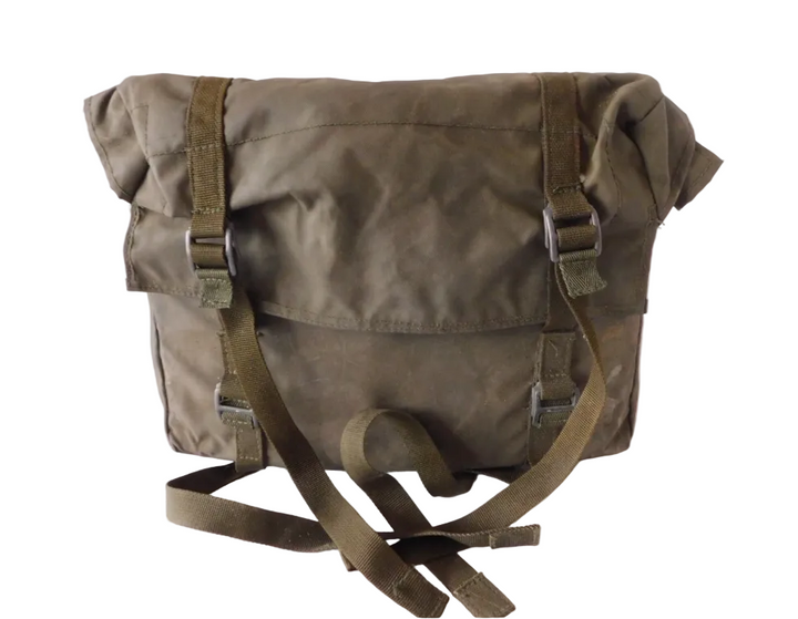 An olive green waxed canvas messenger bag with adjustable straps and a long shoulder strap, resting on a white fabric surface.