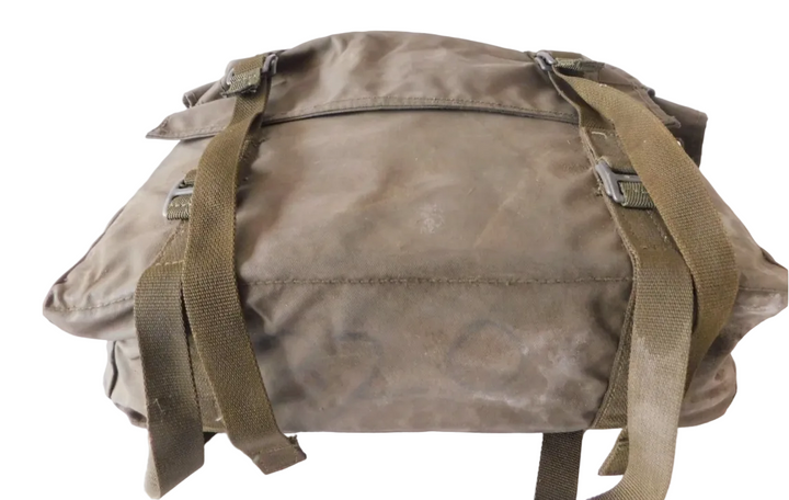 A used olive drab canvas utility bag with adjustable webbing straps and plastic buckles, photographed on a white fabric background.