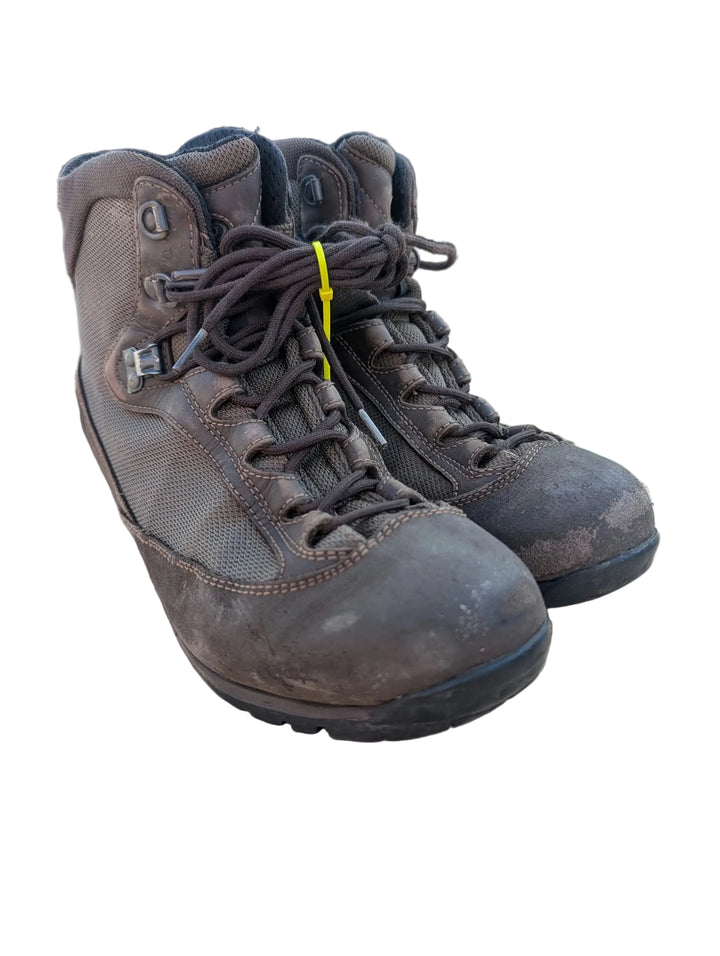 A pair of worn brown lace-up hiking boots placed on a cardboard surface with a reflective tabletop and a dark background.