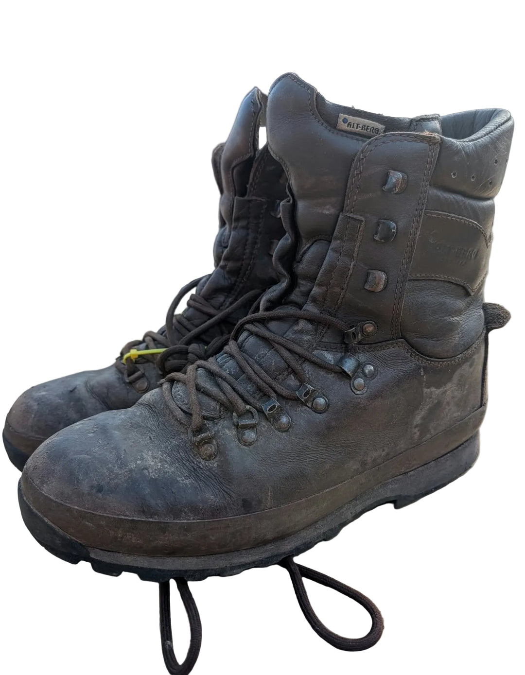 A pair of rugged, dark brown high-top work boots with heavy dirt and wear, resting on a cardboard shipping box in an industrial outdoor setting.