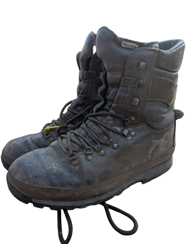 A pair of rugged, dark brown high-top work boots with heavy dirt and wear, resting on a cardboard shipping box in an industrial outdoor setting.