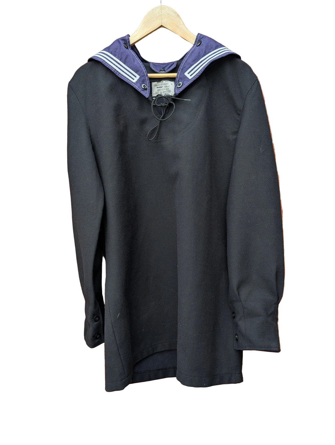 A black long-sleeve sailor-style top with a navy blue collar featuring white stripes, hanging on a wooden hanger against a red brick wall.
