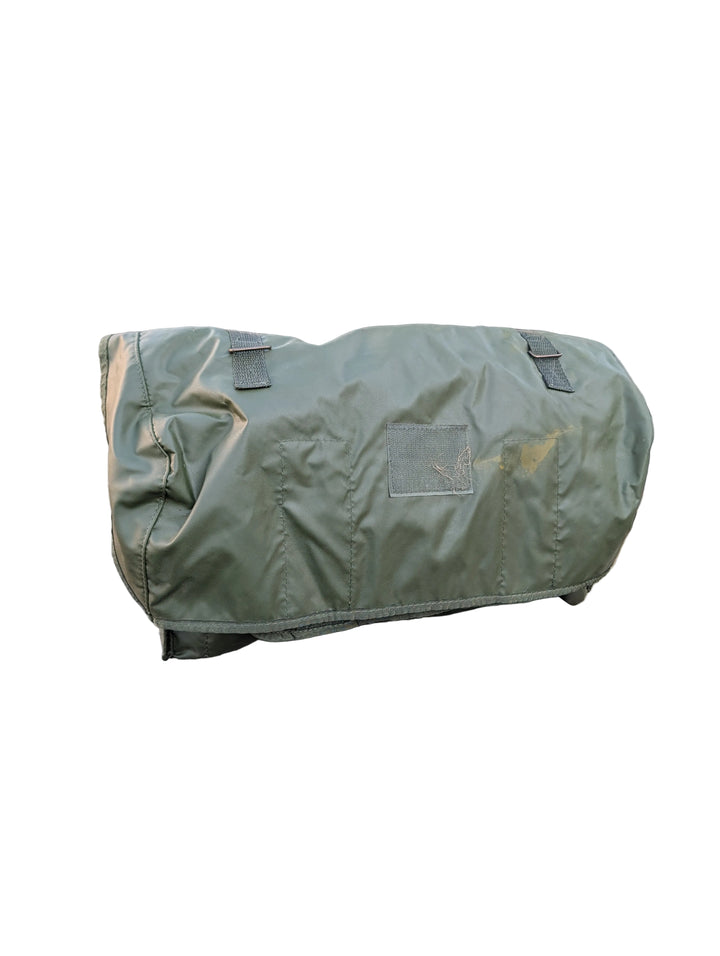 Green military-style duffel bag on a vehicle with a camouflage background