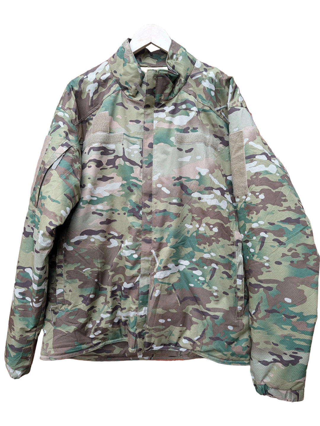 A camouflage military-style jacket hanging on a white hanger against a red brick wall.