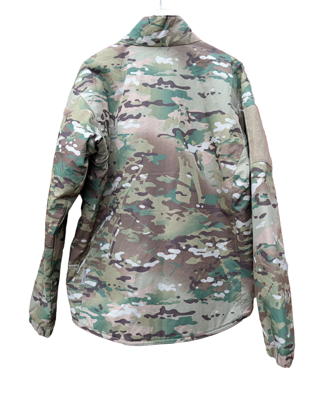 A camouflage military-style jacket hanging on a white hanger against a red brick wall background.
